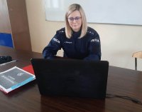 klasa szkolna policjantka siedzi przy biurku przed laptopem, na biurku są rozłożone kartki papieru