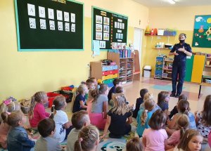 przedszkole policjanta prowadzi prelekcje w klasie, dzieci siedzą na dywanie