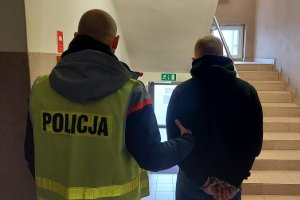 policjant w kamizelce z napisem Policja prowadzi zatrzymanego, korytarz w kutnowskiej komendzie