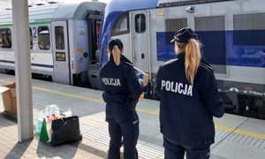 policjantki stoją na peronie, trzymają w ręku kartony ze słodyczami, na tory wjeżdża pociąg