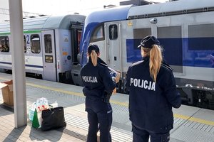 policjantki stoją na peronie, trzymają w ręku kartony ze słodyczami, na tory wjeżdża pociąg