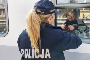 policjantka patrzy na dziecko siedzące w wagonie, dziewczynka rączkami oparte jest o szybe