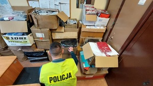 policjant kuca obok pudełek pełnych odzieży torebek butów