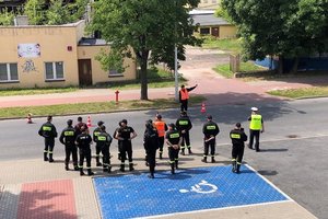 strażacy OSP stają na chodniku policjant stoi na drodze kieruje ruchem