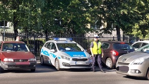 policjant stoi przy radiowozie na parkingu, obok zaparkowane samochody