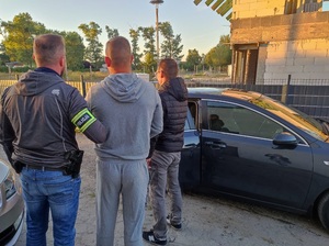 dwóch policjantów na podwórku prowadzą zatrzymanego do samochodu