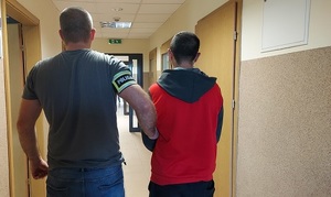 korytarz Komendy Powiatowej Policji w Kutnie, policjant prowadzi zatrzymanego