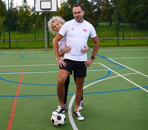 boisko piłkarskie mężczyzna w stroju sportowym stoi nogę trzyma na piłce za nim stoi kobieta