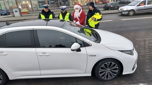 biały samochód policjanci stoją przy kierowcy, mikołaj i mężczyzna w czapce mikołaja