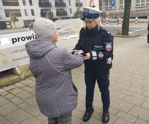 POLICJANTKA ZAKŁADA PIESZEJ OPASKĘ ODBLASKOWĄ NA RĘKĘ.