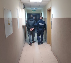 policjant prowadzi korytarzem osobę zatrzymaną.