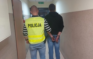policjant prowadzi zatrzymanego mężczyznę korytarzem komendy.