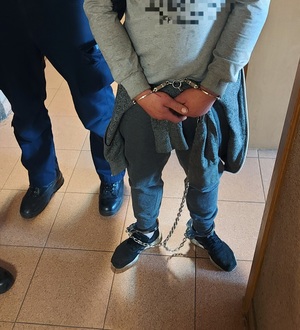 policjant prowadzi zatrzymanego mężczyznę korytarzem komendy.