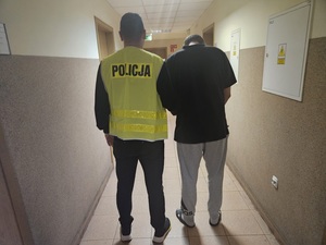 zatrzymany mężczyzna prowadzony przez funkcjonariusza policji.