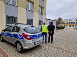 policjant prowadzący zatrzymanego mężczyznę do radiowozu.