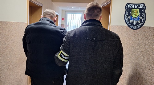 Policjant z zatrzymanym mężczyzną stoją w korytarzu.