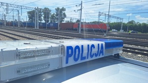 radiowóz policyjny przy torach kolejowych w oddali pociąg towarowy.