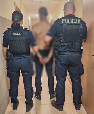 Policjanci stoją z zatrzymanym mężczyzną.