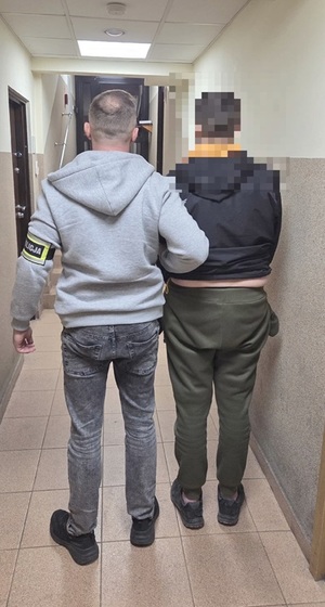 policjant prowadzi zatrzymanego mężczyznę.