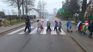 policjantka przeprowadza dzieci przez oznakowane przejście dla pieszych w rejonie szkoły.