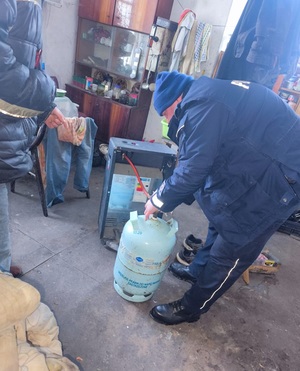 dzielnicowy podłącza butle gazową do piecyka.