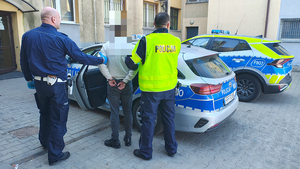 policjanci prowadzą do radiowozu zatrzymanego mężczyznę.
