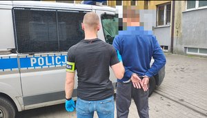 policjant prowadzi zatrzymanego mężczyznę do radiowozu.