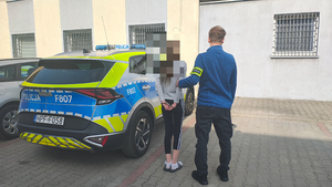 policjant prowadzi zatrzymaną kobietę do radiowozu.