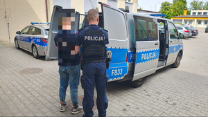 policjant prowadzi zatrzymanego mężczyznę do radiowozu.