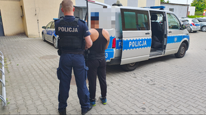 policjant prowadzi zatrzymanego mężczyznę do radiowozu.