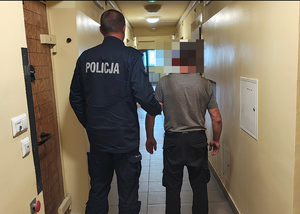 policjant prowadzi zatrzymanego mężczyznę.