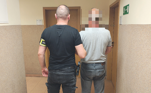 policjant prowadzi zatrzymanego mężczyznę.
