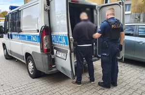 policjant prowadzi zatrzymanego do radiowozu.