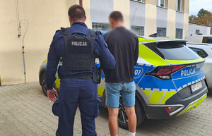 policjant prowadzi zatrzymanego mężczyznę.