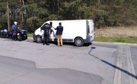 Policjant z Ruchu Drogowego kontroluje kierowcę białego busa, obok redaktor radia Q w ramach akcji rozpoczęcia sezony motocyklowego