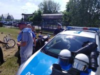 radiowóz policyjny, na nim leży sprzęt  -kaski tarcze , ochraniacze, z tyłu widać policjanta i motocykl nieoznakowany