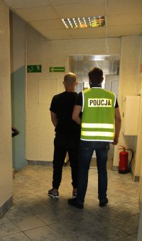 nieumundurowany policjant w kamizelce z napisem POLICJA prowadzi zatrzymanego.