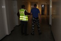 policjant Wydziału Kryminalnego w kamizelce z napisem Policja prowadzi zatrzymanego