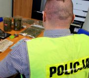 na zdjęciu policjant w kamizelce z napisem policja wraz z zabezpieczonymi narkotykami.