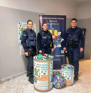 umundurowani policjanci z pojemnikami nakrętek dla podopiecznych hospicjum.