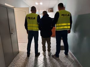 policjanci w kamizelce z napisem POLICJA prowadzą zatrzymanego.