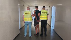 policjanci w kamizelce z napisem POLICJA prowadzą zatrzymanego.
