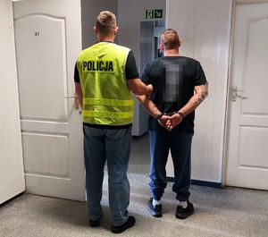 policjant w kamizelce z napisem POLICJA prowadzi zatrzymanego.