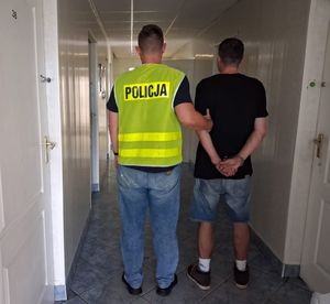 nieumundurowany policjant w kamizelce z napisem POLICJA prowadzi zatrzymanego.