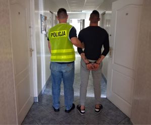 nieumundurowany policjant w kamizelce z napisem POLICJA prowadzi zatrzymanego.