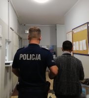 umundurowany policjant prowadzi zatrzymanego po korytarzu w komendzie policji
