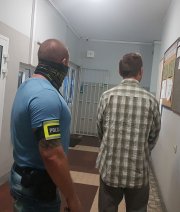 policjant prowadzi zatrzymanego po korytarzu w  budynku jednostki policji