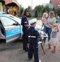 radiowóz stojący w tle oraz policjantka na Jesiennym Pikniku, która przeprowadza quiz wiedzy o bezpieczeństwie wśród uczestników. Całość imprezy odbywa się na na powietrzu.