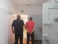 policjant prowadzi zatrzymanego po korytarzu w policyjnym areszcie