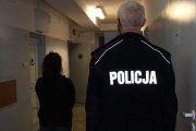 umundurowany policjant prowadzi zatrzymaną do celi w policyjnym areszcie.